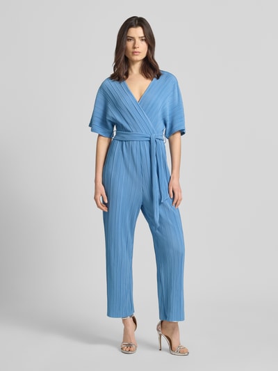 Modelka kobieca nosi Regular Fit Jumpsuit mit V-Ausschnitt model 'Olinda' od YAS w niebieskim kolorze, plisowana faktura, taliowany krój, pasek z materiału, krótki rękaw, długość tyłu w rozmiarze 36: 74 cm, szerokość w rozmiarze 36: 30 cm, długość rękawów w rozmiarze 36: 15 cm, całkowita długość w rozmiarze 36: 143 cm, długość wewnętrzna nogawki w rozmiarze 36: 66 cm, widok całej sylwetki od przodu