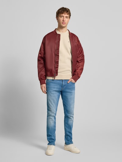 Männermodel trägt Slim Fit Jeans aus Baumwoll-Mix Modell 'SCANTON SLIM' von Tommy Jeans in blauer Denim-Optik, 5-Pocket-Design, Label-Patch, Logo-Stitching, Knopf und verdeckter Reißverschluss, Gürtelschlaufen, Ganzkörperansicht von vorne.