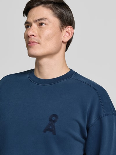 Männermodel trägt Relaxed Fit Sweatshirt aus reiner Bio-Baumwolle Modell 'ICONIC GMT DYE' von Armedangels in Optik: Unifarben, Logo-Stitching, Materialverarbeitung: Sweat, Farbe Blau, Nahaufnahme Oberkörper.