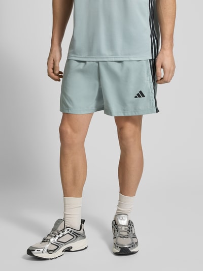 Männermodel trägt Shorts mit elastischem Bund von adidas Training in Hellblau mit Label-Prints, Reißverschlusstaschen, Ganzkörperansicht von vorne.