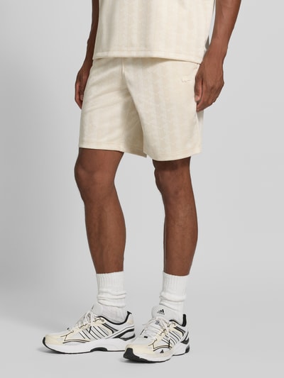 Männermodel trägt cremefarbene Regular Fit Sweatshorts mit Monogramm-Logo-Print von Lacoste, Herren Sweatshorts, Nahaufnahme Beine