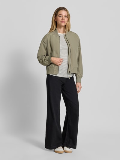 Frauenmodel trägt Regular Fit Jacke mit Stehkragen von camel active in Olivgrün, Zweiwege-Reißverschluss, elastische Abschlüsse, Eingrifftaschen, Ganzkörperansicht von vorne.