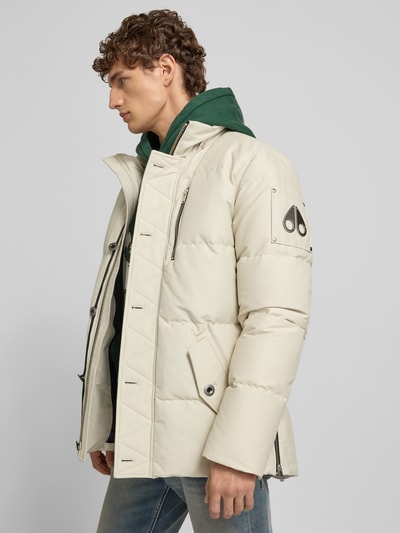 Männermodel trägt Daunenjacke mit Kapuze von Moose Knuckles in Beige, Baumwoll-Mix, Regular Fit, Pattentaschen, Ganzkörperansicht von der Seite