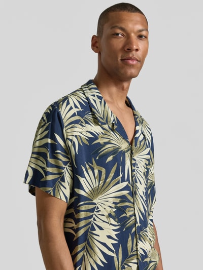 Männermodel trägt Regular Fit Freizeithemd aus reiner Viskose Modell 'BEACH SHIRT' von BOSS mit grünem Beach-Print auf dunkelblau, Nahaufnahme Oberkörper.