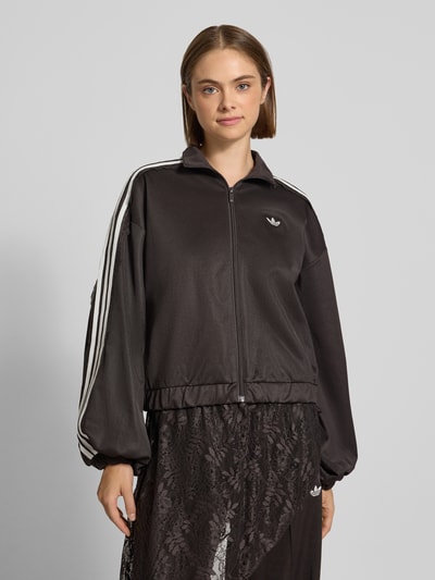 Kobiece modelka nosi czarną bluzę rozpinaną Oversized Sweatjacke aus Baumwoll-Mix model 'LACE OVERSIZED' od adidas Originals z białymi paskami, gładka faktura, prosta forma, widok na cały przód, damska bluza rozpinana.