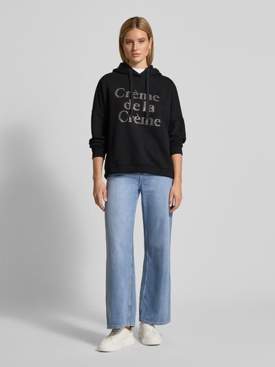 Frauenmodel trägt Oversized Hoodie mit Kapuze von miss goodlife in Schwarz, Schriftzug, gerippte Abschlüsse, Ganzkörperansicht von vorne.