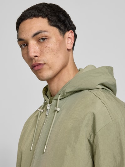 Männermodel trägt Regular Fit Jacke mit Kapuze von WON HUNDRED in heller grünlicher Farbe, Reißverschluss, Tunnelzug, Känguru-Tasche, Nahaufnahme Oberkörper. Rückenlänge bei Größe M 69 cm, Schulterbreite 56 cm, Ärmellänge 63 cm.