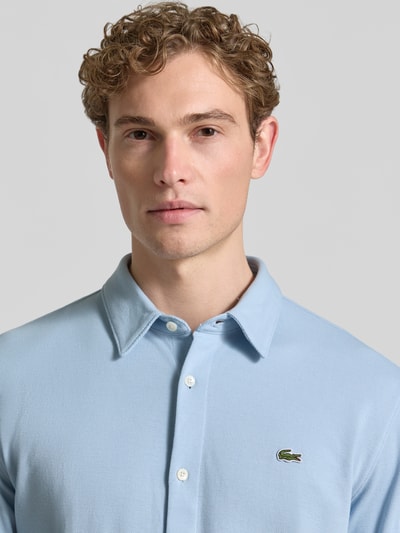 Männermodel trägt Slim Fit Freizeithemd aus reiner Baumwolle von Lacoste in Optik: Unifarben, mit Kentkragen und Logo-Stitching, Nahaufnahme Oberkörper.