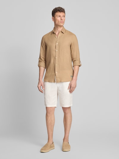 Männermodel trägt Regular Fit Leinenhemd aus zuiver linnen model 'CORE' van Scotch & Soda in bruin met doorlopende knoopsluiting, lange mouwen, labelstitching en kentkraag, gecombineerd met lichte korte broek, context: heren linnen overhemd, ruglengte maat M 78 cm, schouderbreedte 45 cm, mouwlengte 66 cm, ganzkörperansicht van voren.