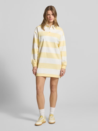 Frauenmodel trägt Regular Fit Minikleid mit Polokragen Modell 'Varsity' von Calvin Klein Jeans aus reiner Baumwolle, gelb-weiße Streifen, Langärmelig, Logo-Stitching, elastische Ärmelabschlüsse, Ganzkörperansicht von vorne.