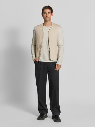 Männermodel trägt Regular Fit Weste mit V-Ausschnitt Modell 'Marve' von Tiger of Sweden in Beige, Zweiwege-Reißverschluss, schwarze Hose, ganzkörperansicht von vorne, moderne Form, glatte Textur, Kontext: Herren Weste mit Reißverschlusstaschen, Rückenlänge 63 cm, Schulterbreite 41 cm, Brustweite 52 cm.