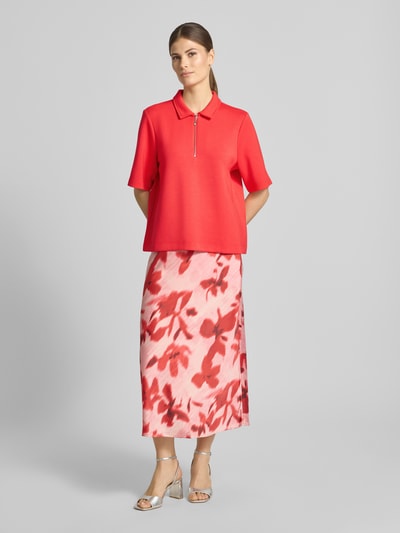 Kobieta nosi Regular Fit Poloshirt mit Reißverschluss von Christian Berg Woman, mieszanka materiałów z domieszką modalu, rękaw o dł. 1/2, kolor czerwony, gładka tekstura. Ganzkörperansicht von vorne.