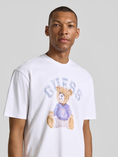 Männermodel trägt T-Shirt mit Motiv-Print und Rundhalsausschnitt von Guess aus reiner Baumwolle im Regular-Fit, Motiv in Pastellfarben, Nahaufnahme Oberkörper.