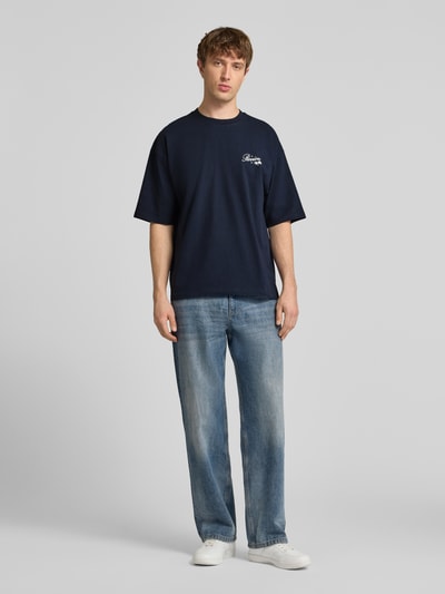 Männermodel trägt T-Shirt mit Rundhalsausschnitt und Label-Print von REVIEW, Reine Baumwolle, Relaxed-Fit, Rückenlänge 71 cm, Ganzkörperansicht von vorne.