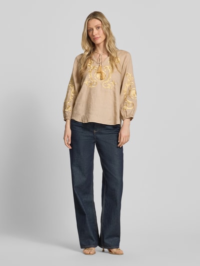Frauenmodel trägt Leinenbluse mit Motiv-Stitching und Quasten-Details von Emily Van den Bergh, beige mit gelb, Loose-Fit, Tunikakragen, elastische Ärmelabschlüsse, reine Leinen, Rückenlänge 64 cm, Ärmellänge 50 cm, Ganzkörperansicht von vorne.