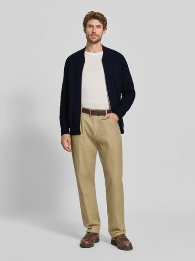 Männermodel trägt Regular Fit Strickjacke aus Baumwoll-Mix mit Kaschmir-Anteil von FTC Cashmere in Dunkelblau, College-Stil, Zweiwege-Reißverschluss, elastische Abschlüsse, kombiniert mit heller Hose, Ganzkörperansicht von vorne.