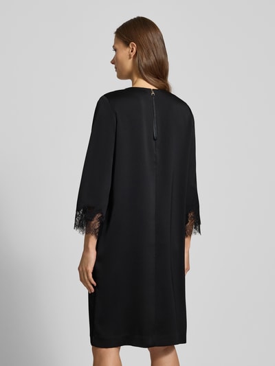 Kobiece modelka ma na sobie sukienkę Knielanges Kleid mit Rundhalsausschnitt Modell 'Dancia' od JOOP!, krój relaxed fit, okrągły dekolt, długość do kolan, rękaw o dł. 3/4, obszycie koronką, długość tyłu 100 cm, szerokość klatki piersiowej 49 cm, długość rękawów 65 cm, kolor czarny, gładka tekstura, delikatne koronki na rękawach. Ganzkörperansicht Rückansicht.