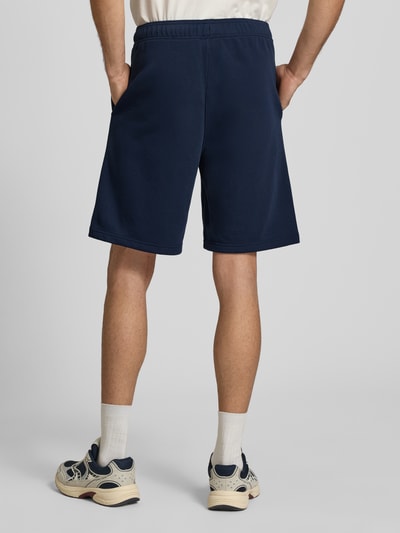 Männermodel trägt Bermudas mit elastischem Bund und Label-Stitching von CHAMPION in Dunkelblau, Baumwoll-Mix, Regular Fit, Ganzkörperansicht Rückansicht.