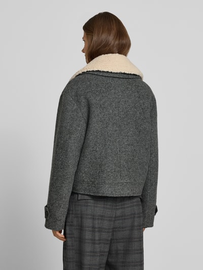 Frauenmodel trägt Jacke mit Kentkragen und Eingrifftaschen von Style Icon Collection, graue Farbe, strukturierte Oberfläche, Ganzkörperansicht Rückansicht. Gerader Schnitt, Knopfleiste, seitliche Eingrifftaschen, Ärmelriegel mit Knopf, Rückenlänge 54 cm, Schulterbreite 52 cm, Brustweite 50 cm, Ärmellänge 60 cm.