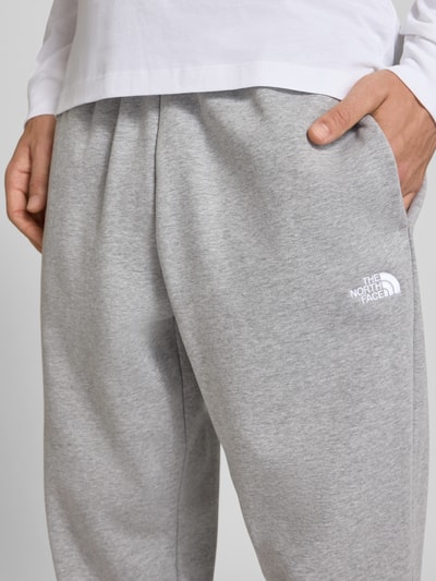 Männermodel trägt graue Relaxed Fit Sweatpants aus katoenmix Modell 'EVOLUTION' von The North Face mit steekzakken, detailaufnahme, Heren sweatpants, elastische band met tunnelkoord, binnenbeenlengte maat M 75 cm.