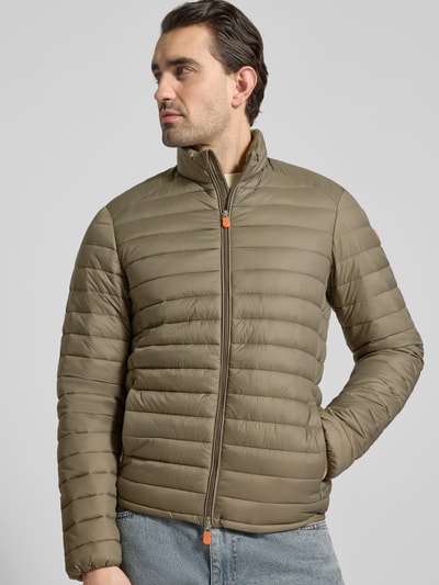 Männermodel trägt olivgrüne Steppjacke mit Zweiwegereißverschluss Modell 'Alexander' von SAVE THE DUCK, Stepp-Optik, Regular Fit, gefütterter Stehkragen, Eingrifftaschen mit Reißverschluss, Ganzkörperansicht von vorne.