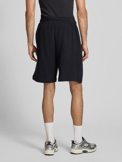 Männermodel trägt Regular Fit Shorts mit elastischem Bund von KARL KANI aus reiner Baumwolle mit Strukturmuster, Ganzkörperansicht Rückansicht.