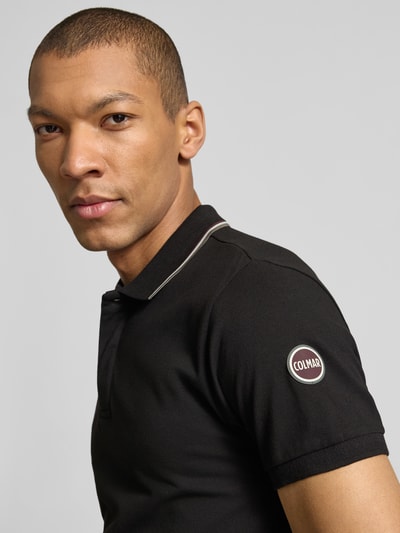 Männermodel trägt Slim Fit Poloshirt aus Baumwolle von Colmar Originals in Schwarz mit Label-Details, Nahaufnahme Oberkörper.