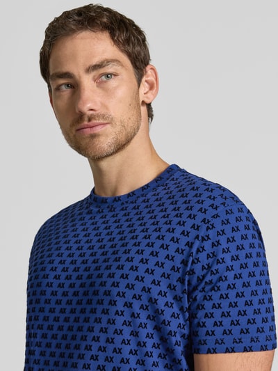 Męski model nosi Regular Fit T-Shirt mit Allover-Print od Armani Exchange, okrągły dekolt, krój regular fit, nadruk na całej powierzchni, z krótkim rękawem, długość tyłu w rozmiarze M: 63 cm, zbliżenie na górną część ciała