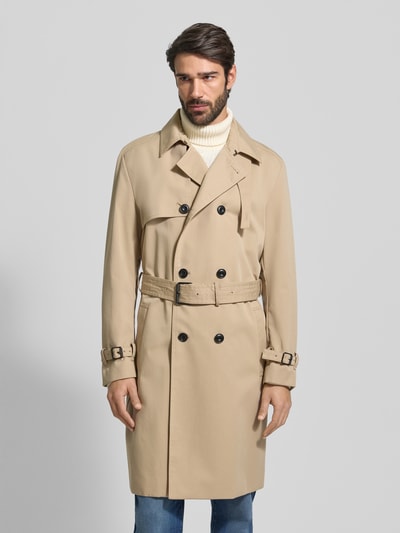 Männermodel draagt Regular Fit Trenchcoat met Gun Flap model 'MALUKS2511' van HUGO in effen kleuren, dubbele knoopsluiting, tailleriem, loopsplit, labelstitching, waterafstotend, steekzakken, binnenzak, platte kraag, lange mouwen, achterpas; Ganzkörperansicht van voren.