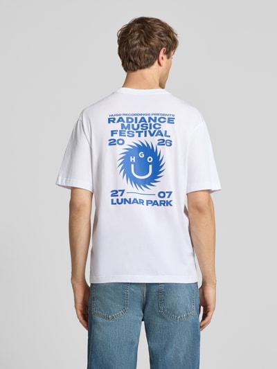 Männermodel trägt Regular Fit T-Shirt aus reiner Baumwolle Modell 'Nunarix' von HUGO in Optik: Unifarben, Label-Print, Weiß und Blau, Materialverarbeitung: Jersey, Ganzkörperansicht Rückansicht.