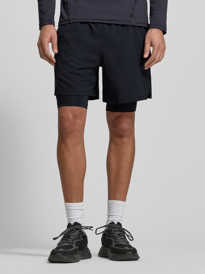Männermodel trägt Regular Fit Shorts mit integrierten Tights Modell 'Vanish' von Under Armour in Schwarz, Logo-Print, elastischer Bund, Eingrifftaschen, Ganzkörperansicht von vorne.