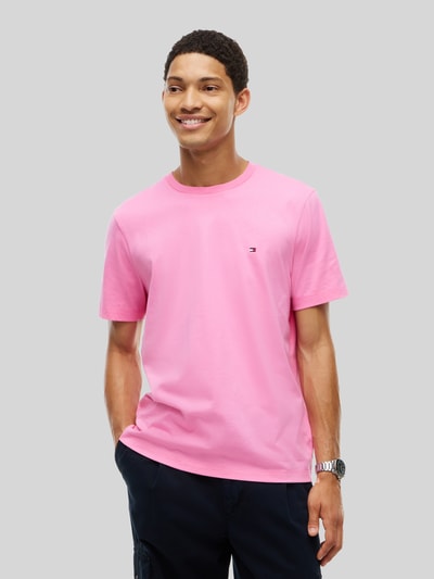 Männermodel trägt Regular Fit T-Shirt aus reiner Baumwolle von Tommy Hilfiger in Rosa, dezentes Markenlogo, Ganzkörperansicht von vorne.