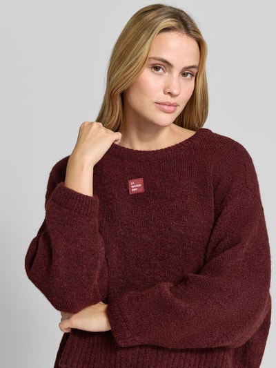 Frauenmodel trägt Oversized Pullover mit Alpaka-Anteil Modell 'East' von American Vintage in Bordeaux, Strick-Optik, Nahaufnahme Oberkörper.