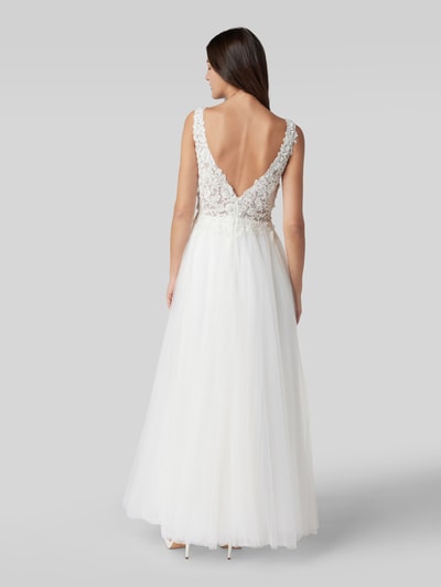 Kobiece modelka nosi Brautkleid mit Ziersteinen und floraler Spitze od Mascara w kolorze białym, taliowany fason, dekolt w serek, szerokie ramiączka, ozdobne kamienie, półprzezroczysty materiał wierzchni, halka pod sukienkę, wszyty zamek błyskawiczny i zapięcie na haftkę, długość tyłu w rozmiarze 36: 150 cm, szerokość klatki piersiowej w rozmiarze 36: 39 cm, całopostaciowy widok z tyłu.