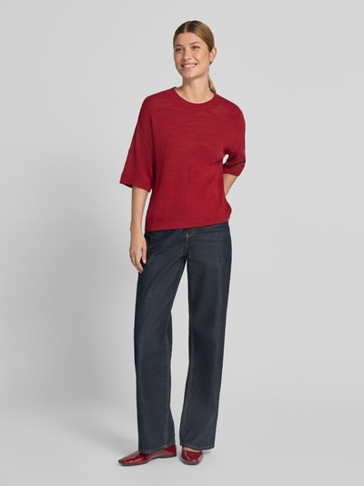 Vrouwenmodel draagt gebreid shirt met 1/2-mouwen Model 'Lauralynn' van MSCH Copenhagen, mix van biologisch katoen, loose fit, ronde hals, schouderpartijen, ruglengte maat S/M 53 cm, mouwlengte maat S/M 22 cm, donkerrood, blauwe broek, rode schoenen, geheelfiguur van voren