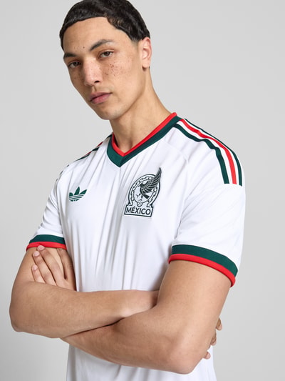 Männermodel trägt Auswärtstrikot Mexico 2026 von adidas Sportswear, mehrfarbig, Slim-Fit, V-Ausschnitt, Kurzarm, Logo-Applikation, Nahaufnahme Oberkörper.