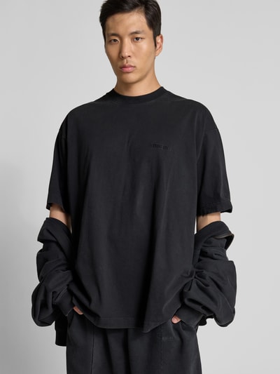 Männermodel trägt Oversized T-Shirt aus Reiner Baumwolle von VETEMENTS in Schwarz mit Rundhalsausschnitt und Label-Stitching, Nahaufnahme Oberkörper.