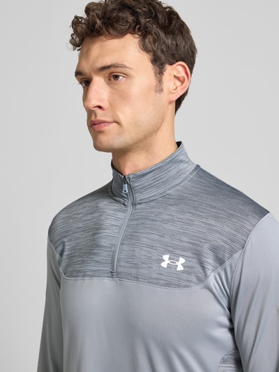 Männermodel trägt Sweatshirt mit Stehkragen von Under Armour in Grau mit kurzem Reißverschluss, Label-Print, Nahaufnahme Oberkörper. Rückenlänge 73 cm, Ärmellänge 72 cm bei Größe L, Slim Fit.