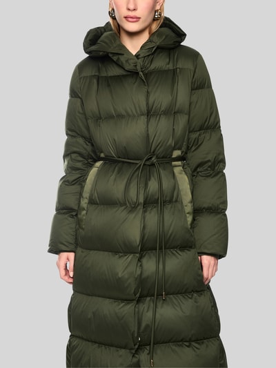 Frauenmodel trägt Steppmantel mit Bindegürtel von Marc Cain in Olivgrün, Kapuze und Bindegürtel, Regular Fit, Nahaufnahme Oberkörper. Rückenlänge 107 cm, Schulterbreite 43 cm, Brustweite 58 cm, Ärmellänge 63 cm.