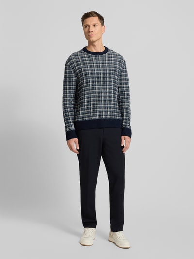 Männermodel draagt Regular Fit Strickpullover aus Woll-Mix Modell 'MIKOLAS' van SELECTED HOMME met blauw-wit ruitpatroon, geribde boorden, allover-motief, lange mouwen, gebreide textuur, Ganzkörperansicht von vorne.