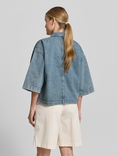 Frauenmodel trägt Jeansjacke mit Kimonoärmeln Modell 'ZOE' von Mustang aus Reine Baumwolle, Regular-Fit, Umlegekragen, Schnürverschluss, Seitliche Eingrifftaschen, Rückenlänge bei Größe S 56 cm, Schulterbreite 44 cm, Brustweite 54 cm, Ärmellänge 43 cm, ganzkörperansicht Rückansicht.