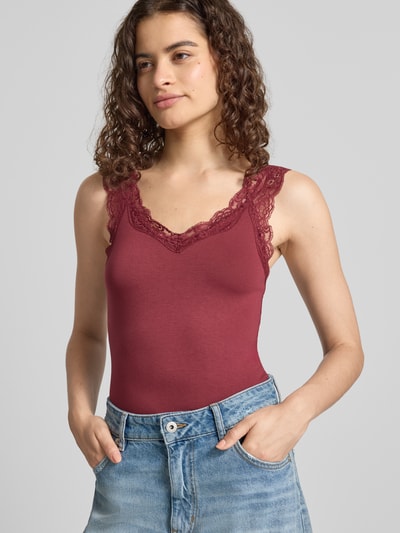 Frauenmodel trägt Slim Fit Tanktop aus Viskose-Mix Modell 'BARBERA' von PIECES in Dunkelrot mit Spitzenbesatz, glatte Textur, Nahaufnahme Oberkörper.