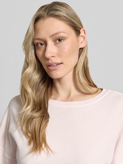Modelka nosi Relaxed Fit T-Shirt aus reiner Baumwolle od s.Oliver RED LABEL, jasnoróżowy kolor, bawełniana faktura, nadruk logo, uniwersalny wygląd, dekolt okrągły, krótkie rękawy, ramka z rolowanym brzegiem, materiał: czysta bawełna, zbliżenie górnej części ciała.