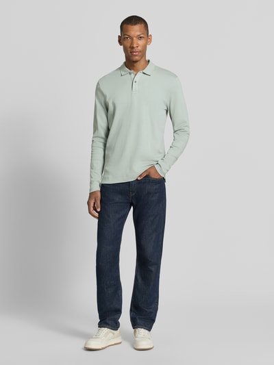 Männermodel trägt Regular Fit Poloshirt aus reiner Baumwolle von Christian Berg Men in Hellgrün, dunkle Jeans, Ganzkörperansicht von vorne.