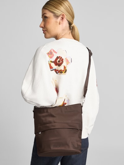 Frauenmodel trägt Handtasche mit Logo-Applikation Modell 'Heather' von BOGNER in Dunkelbraun, glatte Oberfläche, Kontext: Damen Handtasche, Hauptfach mit Reißverschluss, Schulterriemen mit Logo-Detail, Maße: Breite 31 cm, Länge 29 cm, Tiefe 13 cm, Schulterriemen 60 cm, Ganzkörperansicht Rückansicht.