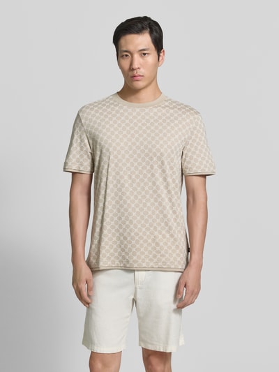 Männermodel trägt T-Shirt mit Logo-Muster und Rundhalsausschnitt von JOOP! Collection aus Baumwoll-Lyocell-Mix in Regular-Fit, Beige-Töne, glatte Textur, Rückenlänge bei Größe M 69 cm, Ganzkörperansicht von vorne.