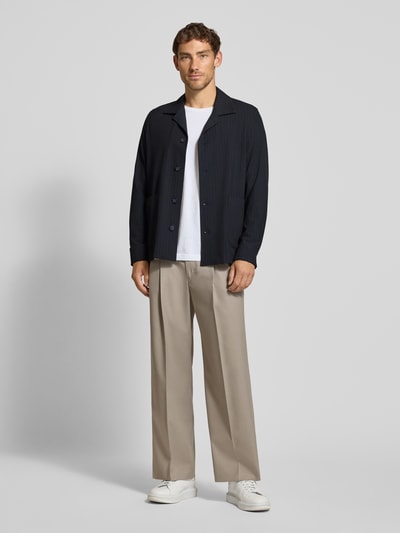 Männermodel trägt Oversized Fit Freizeithemd mit Viskose-Anteil Modell 'Malte' von CINQUE, dunkelblau, beige Hose, weiße Schuhe, Ganzkörperansicht von vorne. Elastischer Material-Mix, Reverskragen, langärmelig, Rückenlänge 75 cm bei Größe M.