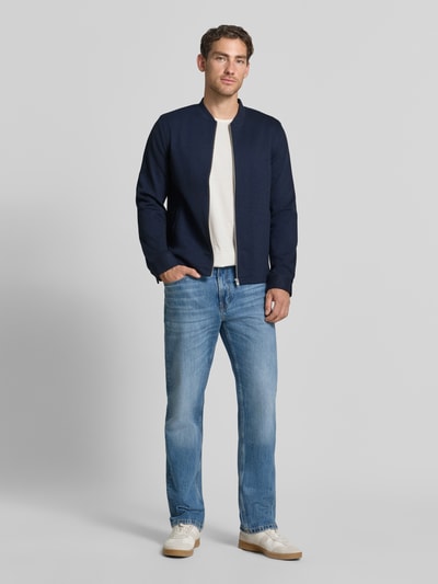 Mężczyzna nosi Slim Fit Sweatjacke mit Stehkragen od Lindbergh, Mieszanka materiałów z dodatkiem streczu, zamek błyskawiczny, wpuszczane kieszenie, długość tyłu w rozmiarze M 67 cm, długość rękawów w rozmiarze M 66 cm, kolor granatowy, prosty fason, widok całej sylwetki z przodu.