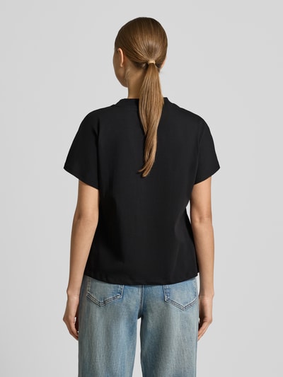 Młodzieżowy modelka nosi Regular Fit T-Shirt mit Ziersteinbesatz Modell 'Popcorn' od Guess, czarna bawełna, krój regular fit, nadruk, okrągły dekolt, długość tyłu 56 cm w rozmiarze S, zdjęcie całej sylwetki z tyłu.