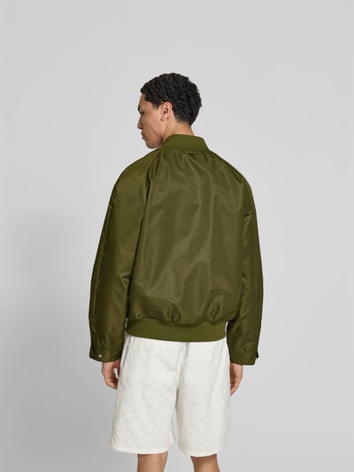 Männermodel trägt Bomberjacke mit Stehkragen von Filippa K in Olivgrün, Relaxed-Fit, elastischer Bund, Eingrifftaschen, Ganzkörperansicht Rückansicht.